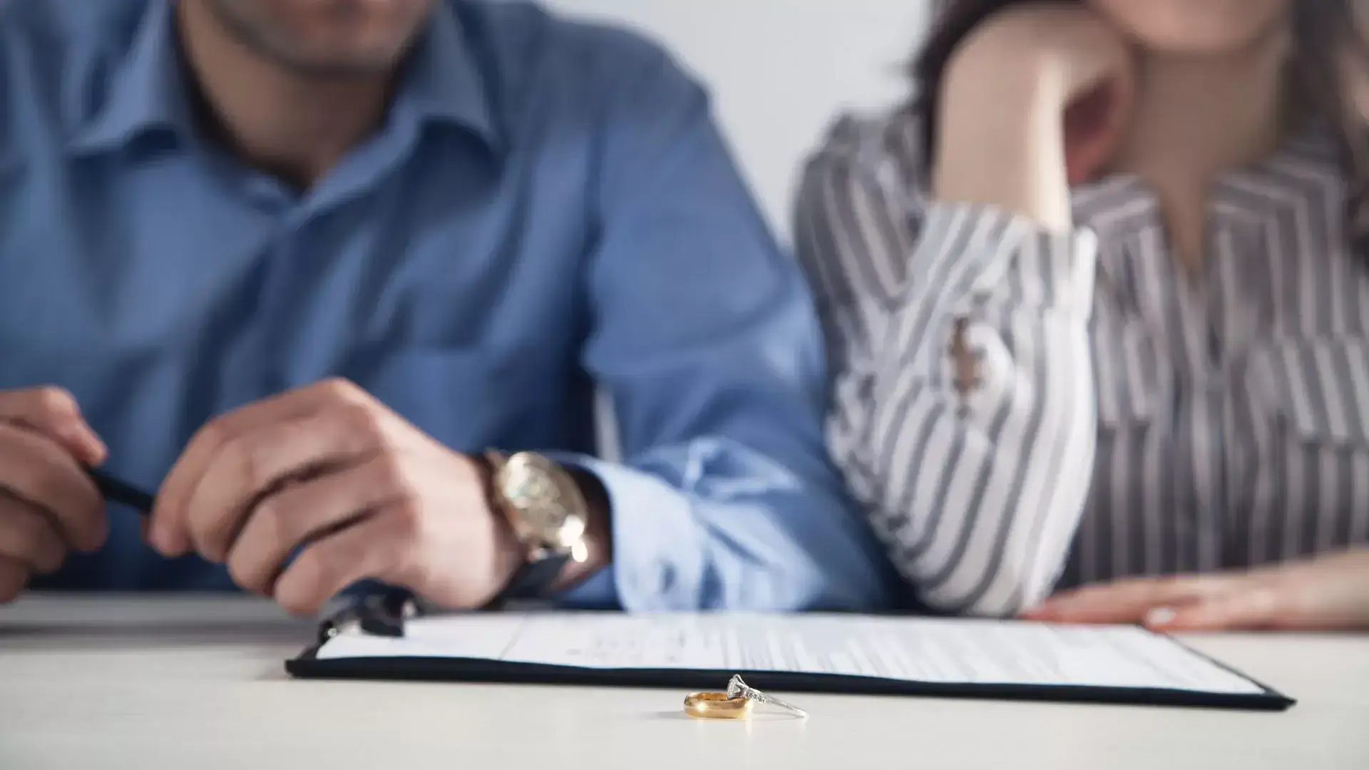 Man holding a pen while reviewing documents with his partner, with a wedding ring on the table during a Grief and Closure Therapy session at Mississauga Divorce Counselling Therapy, addressing the emotional finality of divorce.