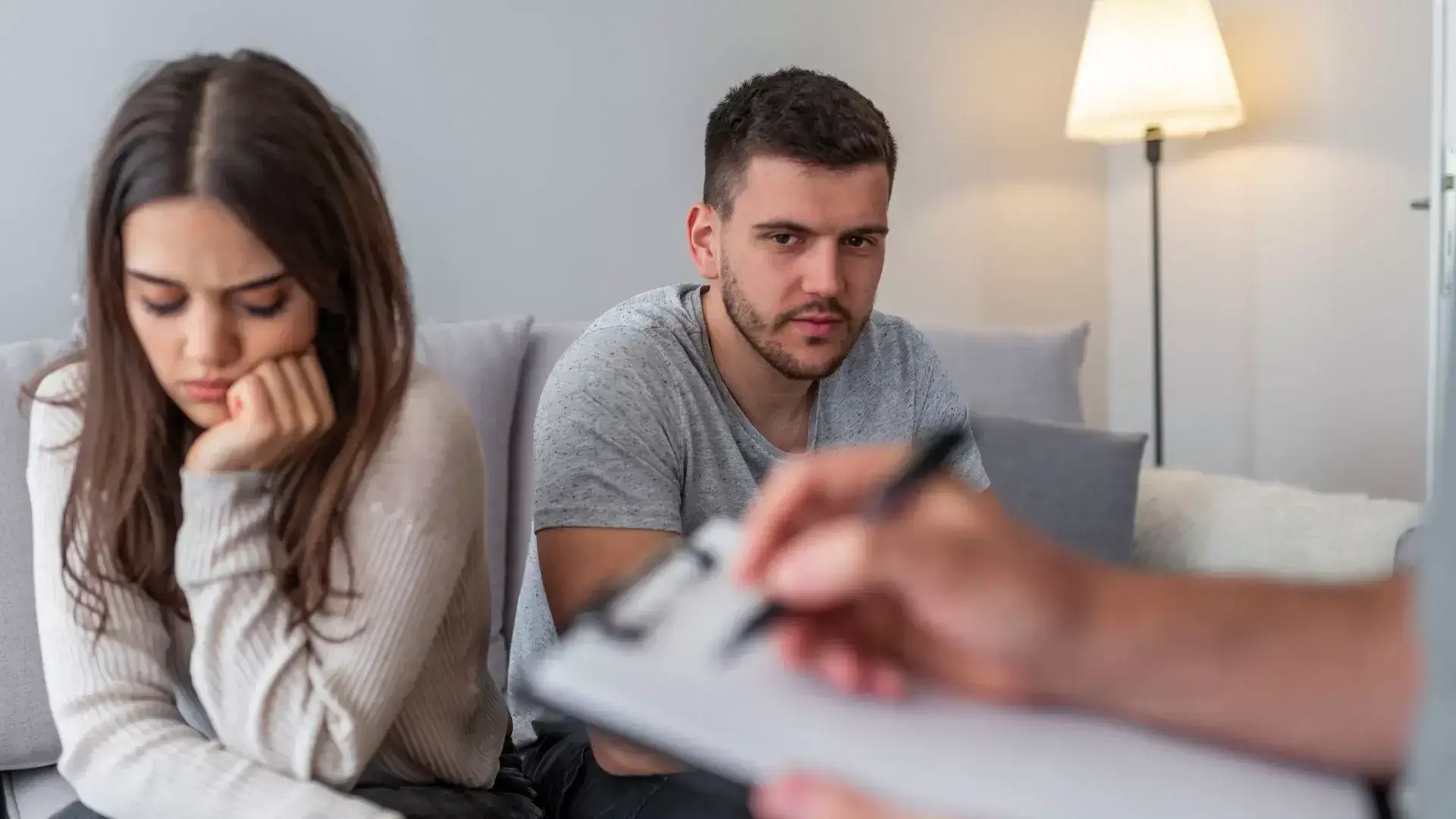 Upset woman turning away from her partner during a Cognitive-Behavioral Therapy session at Oakville Divorce Counselling Therapy, while the man focuses on the therapist’s notes—illustrating how CBT helps manage emotional reactions and improve communication during and after divorce.